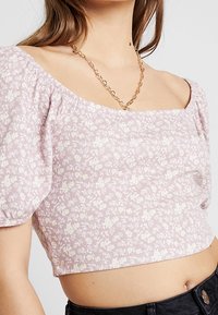 Světle růžový květinový crop top s vypouklými krátkými rukávy, texturovanou tkaninou, čtvercovým výstřihem a přiléhavým střihem. Znatelné detaily květinového vzoru.