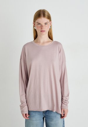 Langermet, lys rosa skjorte laget av mykt stoff, med rund hals og avslappet passform, sammen med lyseblå jeans.