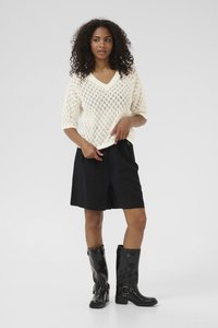 Strickpullover in Creme mit V-Ausschnitt und Rautenmuster, kombiniert mit schwarzen Shorts und kniehohen schwarzen Stiefeln mit Schnallen.
