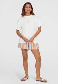 White cotton t-shirt with short sleeves and a yellow graphic, paired with multicolored striped shorts in orange, blue, and gray. Brown sandals.
