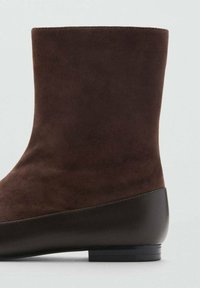 Brown suede ankle boot with a smooth dark brown leather accent, featuring a rounded toe and low black heel. Simple, contemporary design.