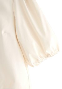 Cremefarvet bluse med puffede ærmer og elastisk manchet. Glat stof med en diskret glans og en diskret sidelomme.