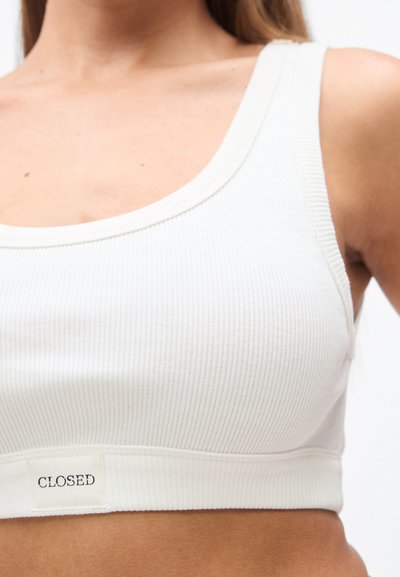 Λευκό ριμπ κοντό σουτιέν με φαρδιά λαιμόκοψη και κάτω ταινία με ετικέτα που γράφει "CLOSED". Μαλακή υφή υφάσματος.