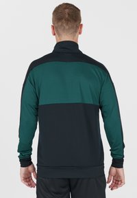 Mörkgrön och svart atletisk tröja med hög krage, långa ärmar och textil med strukturerad yta som har kontrasterande färgpaneler.