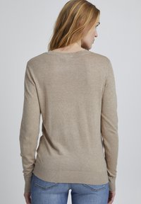 Beige pitkähihaine neulepaita, jossa on pyöreä pääntie, ribbireunat hihoissa ja helmassa, pehmeä rakenne ja löysä istuvuus.