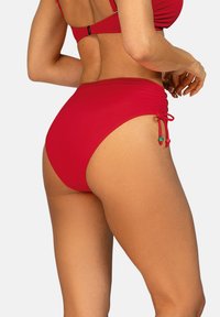 Czerwone, wysokie majtki bikini z teksturowanej tkaniny, wyposażone w regulowane boczne sznurki z dekoracyjnymi koralikami.