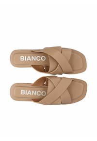 Sandali beige con cinturini incrociati realizzati in materiale sintetico liscio, con una morbida soletta e design a punta quadrata. Logo "BIANCO" in bianco.