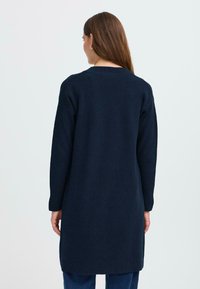 Cardigan marine à manches longues avec une coupe droite, en tissu tricoté texturé et un col rond, s'étendant jusqu'à mi-cuisse.