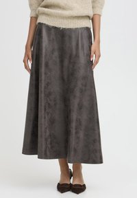 Longue jupe grise foncée en tissu lisse, avec un léger éclat et une silhouette fluide ; portée avec un pull léger et texturé et des chaussures marron.