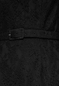 Schwarzer Spitzenstoff mit einem strukturierten Design, mit einem schwarzen Gürtel und einer Metallschnalle, in einer Nahaufnahme dargestellt.