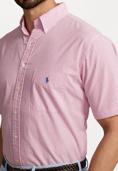 Īsām piedurknēm, pogājama krekls rozā un baltās svītrās, ar kreisajā krūtī esošu kabatu un mazu zilu logotipu. Izgatavots no viegla auduma.