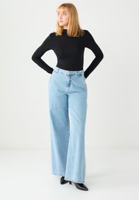 Jasnoniebieskie dżinsy z wysokim stanem i szerokimi nogawkami, zapięte z przodu na guziki, z bocznymi kieszeniami, noszone z czarną bluzką z długim rękawem.