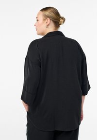 Čierna voľná blúzka s golierom, trojštvrťovými rukávmi a mäkkou textúrovanou látkou. Prispôsobený zakrivený spodný lem na zadnej strane.