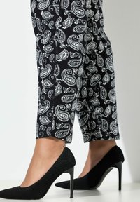 Černé vysoké podpatky s vroubkovanou texturou a špičatými špičkami, spárované s černo-bílými kotníkovými kalhotami s paisley vzorem.