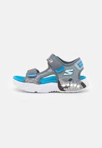Grå og blå sportsandaler med justerbare stropper, nettdesign, teksturert innersåle og haifigur med lyse detaljer på sålen.