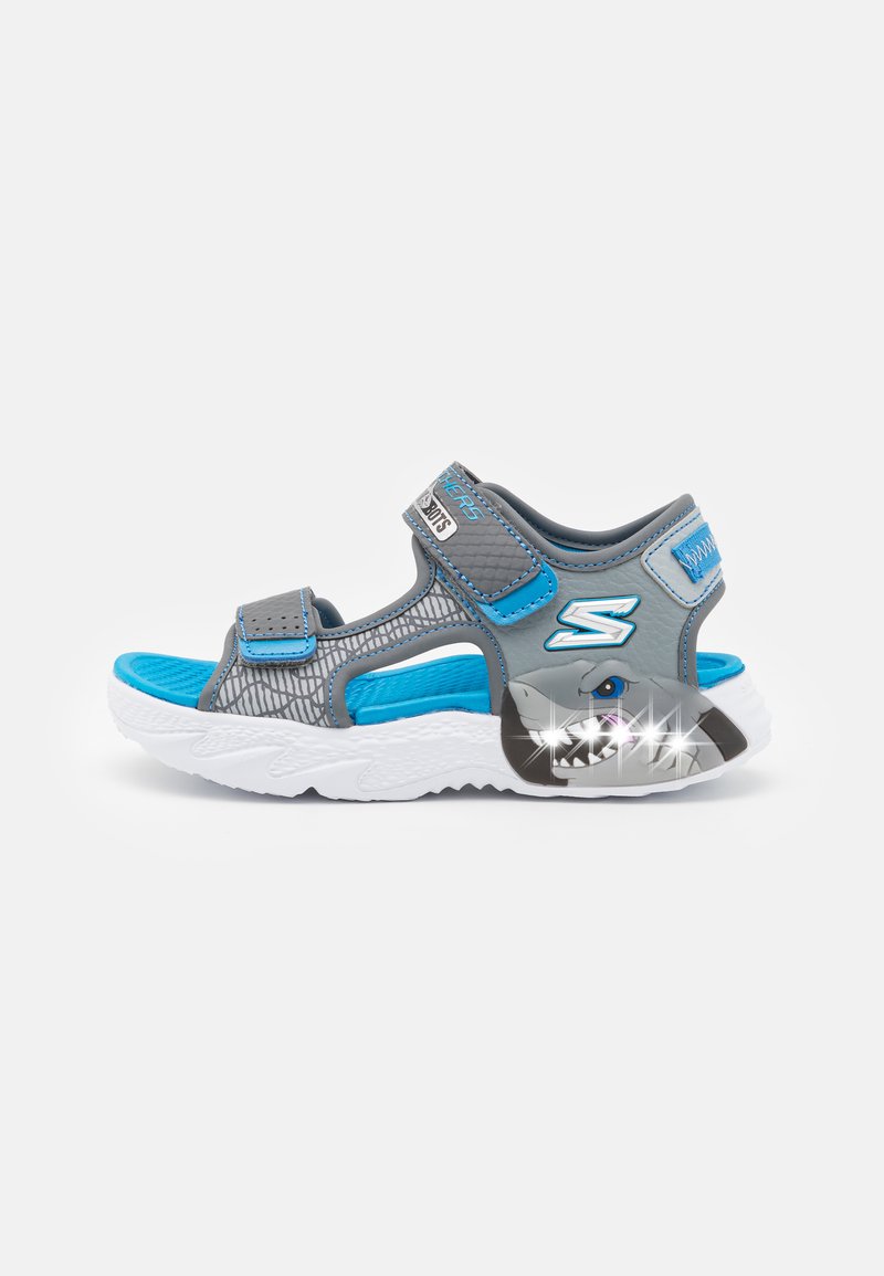 Grå og blå sportsandaler med justerbare stropper, nettdesign, teksturert innersåle og haifigur med lyse detaljer på sålen.
