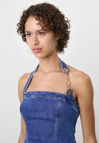 Denim kjole med firkantet udskæring og halterneck stropper, med en guld kædedetalje på den ene skulder, i en mellemblå vask.