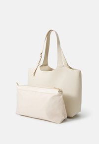 Beigenvärinen nahkainen olkalaukku, jossa on kaksi kahvaa ja erillinen, vaaleanbeige vetoketjullinen pussukka. Sileä pinta, minimalistinen muotoilu ja hillityt metallikoristeet.