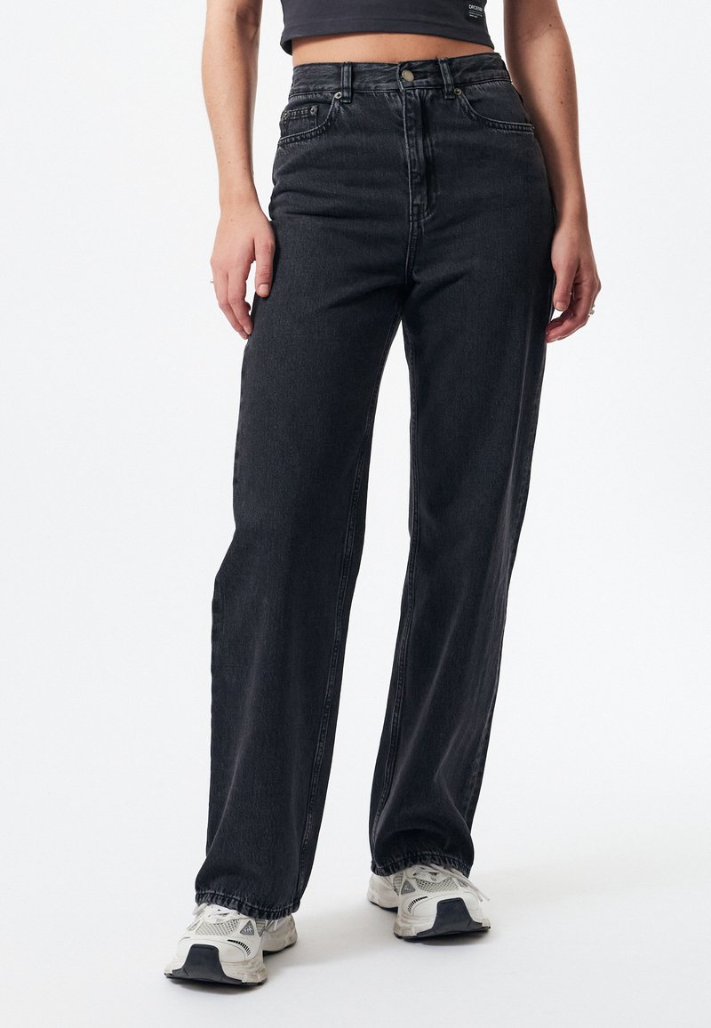 High-waisted black denim jeans with a straight-leg design, featuring a button closure and subtle stitching details, paired with white sneakers.