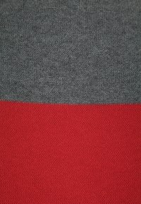 Texturerat tyg med en horisontell delning; överdelen är mörkgrå och underdelen är livfullt röd, båda i stickat material.