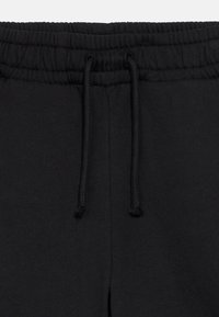 Sorte joggingbukser med snøre i taljen, blødt bomuldsmateriale og en tekstureret overflade. Glat stof med elastiske manchetter.