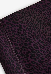 Lila tyg med ett svart leopardmönster och slät yta. Inkluderar mörka sömmar längs kanterna som framhäver designen.