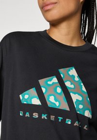 Zwarte T-shirt met korte mouwen met een grote grafische afbeelding van turquoise en beige luipaardprint en de tekst "BASKETBAL" eronder.