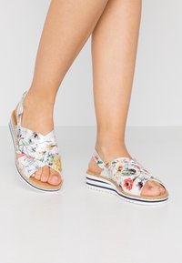 Blommönstrade sandaler med en silverfärgad bas, överlappande remmar, korkfotbädd och vit gummisula med marinblå ränder.