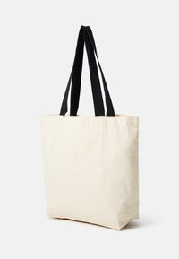 Sac en toile crème avec des poignées en tissu noir. Forme rectangulaire, coutures solides, texture lisse sans motifs ni accents.