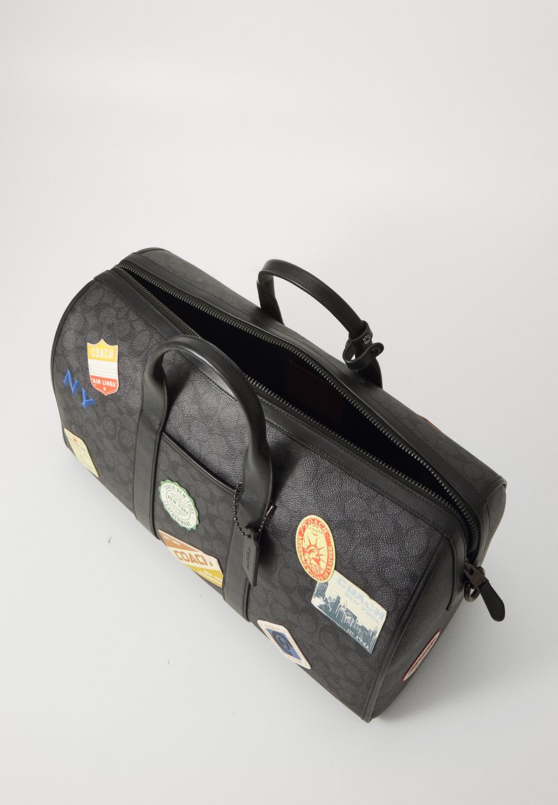Black leather duffel bag featuring various travel stickers, round shape, dual handles, and a top zipper closure with textured surface.