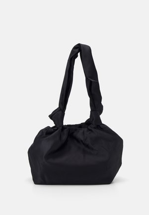 Bolso de tela negro con un asa anudada, de forma redondeada y textura suave. El diseño es sencillo, sin herrajes ni acentos visibles.