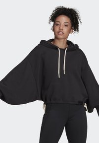 Felpa nera oversize con maniche ampie, cappuccio con cordino e lacci in crema a contrasto, abbinata a leggings neri. Tessuto morbido e liscio.