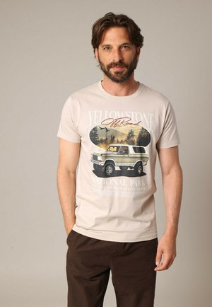 Beige katoenen T-shirt met een grafische print van een vintage truck in Yellowstone National Park, omringd door bomen en landschapsillustraties.