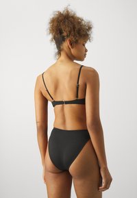 Svart bikini-set med en enkel design, justerbara axelband och högar bas. Materialet verkar slätt med minimala detaljer i hårdvara.