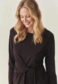 Vestido negro de manga larga con detalle de nudo retorcido en la cintura, hecho de una tela suave. El diseño presenta una silueta relajada.