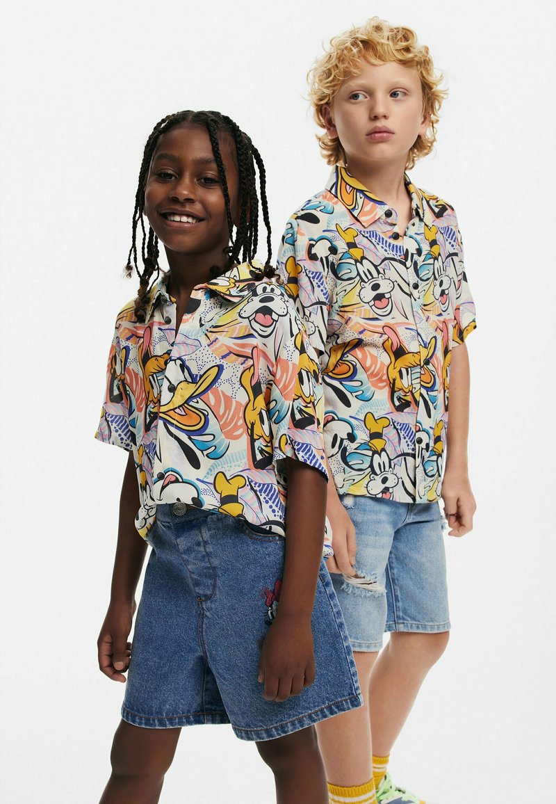 Le magliette a maniche corte, colorate, presentano personaggi dei cartoni animati e motivi astratti, abbinate a pantaloni corti in denim e calzini e scarpe multicolori.