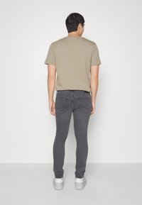 Jeans grises de corte ajustado con dos bolsillos traseros, combinados con una camiseta de algodón beige de manga corta. Zapatillas blancas completan el atuendo.