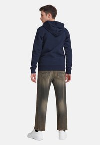 Felpa blu navy con tasca a marsupio, abbinata a jeans marroni sbiaditi a gamba larga. Scarpe da ginnastica bianche completano l'outfit.