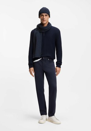 Granatowy sweter z dzianiny z wysokim kołnierzem, zestawiony z granatowymi spodniami i białymi trampkami. Charakteryzuje się dopasowanym fasonem i pasującym szalikiem.