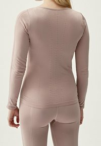 Långärmad träningsöverdel i mjuk rosa tyg, med ribbat mönster, vertikala linjedetaljer och diskreta perforeringar längs ryggen.