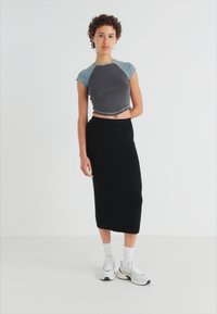 Crop top gris ajusté à manches courtes associé à une jupe midi noire, porté avec des chaussettes blanches à la cheville et des baskets grises. Texture de tissu lisse.