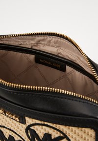 Svart och beige väska med flätad struktur. Guldfärgad dragkedjedetalj och satinfoder. Läderdetaljer och synlig varumärkesetikett "Michael Kors."