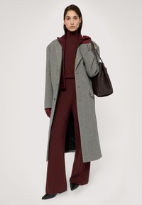Szary wełniany płaszcz o długiej sylwetce, uzupełniony burgundowym golfem i pasującymi szerokimi spodniami. Dodatki obejmują czarną torbę.