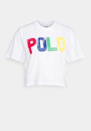 Bílé krátké tričko s velkým nápisem "POLO" v červených, modrých, zelených a žlutých opotřebovaných písmech přes přední stranu.