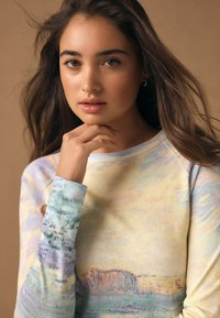 Pikad varrukad särgiga, millel on pehme pastellvesivärvi muster sinise ja kollase toonides, lõdva lõikega ja mansettidega varrukad.