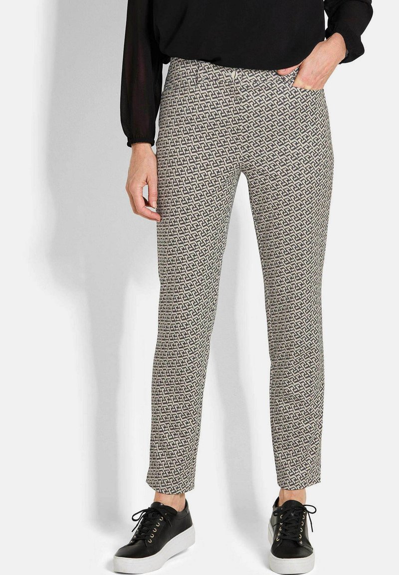 Patronenbroek in crème en zwart, met een geometrisch ontwerp, slanke pasvorm en standaard taille. Gecombineerd met zwarte sneakers.