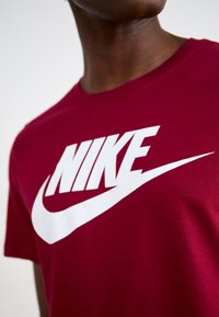 Camiseta de algodón roja con cuello redondo que presenta un gran logo y gráfico en blanco de "NIKE" y su swoosh impreso en la parte frontal.