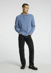 Blue knitted pullover with a collared neckline and three buttons, paired with black pants and black shoes, on a neutral background.