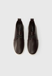 Prunade nahkkingad sujuva tekstuuriga, ümmarguse varbaga ja valge kummitaldaga. Omab tumedaid paelu ja tõmbevahtu kandadel.