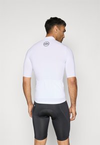 Maillot de cyclisme ajusté à manches courtes en blanc avec un logo circulaire au dos. Associé à un short de cyclisme noir rembourré.